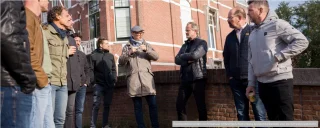 Tien mannen staan buiten en luisteren naar een persoon